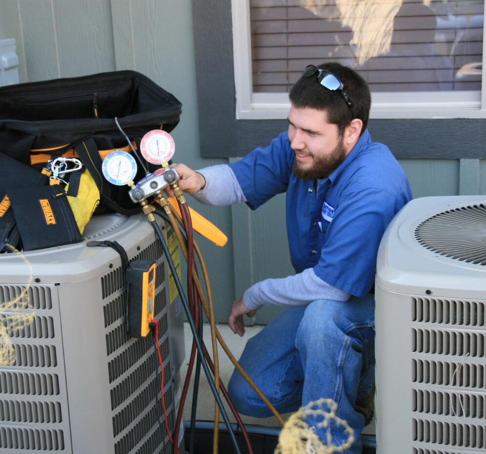 An HVAC tech using gauges working on an AC unit